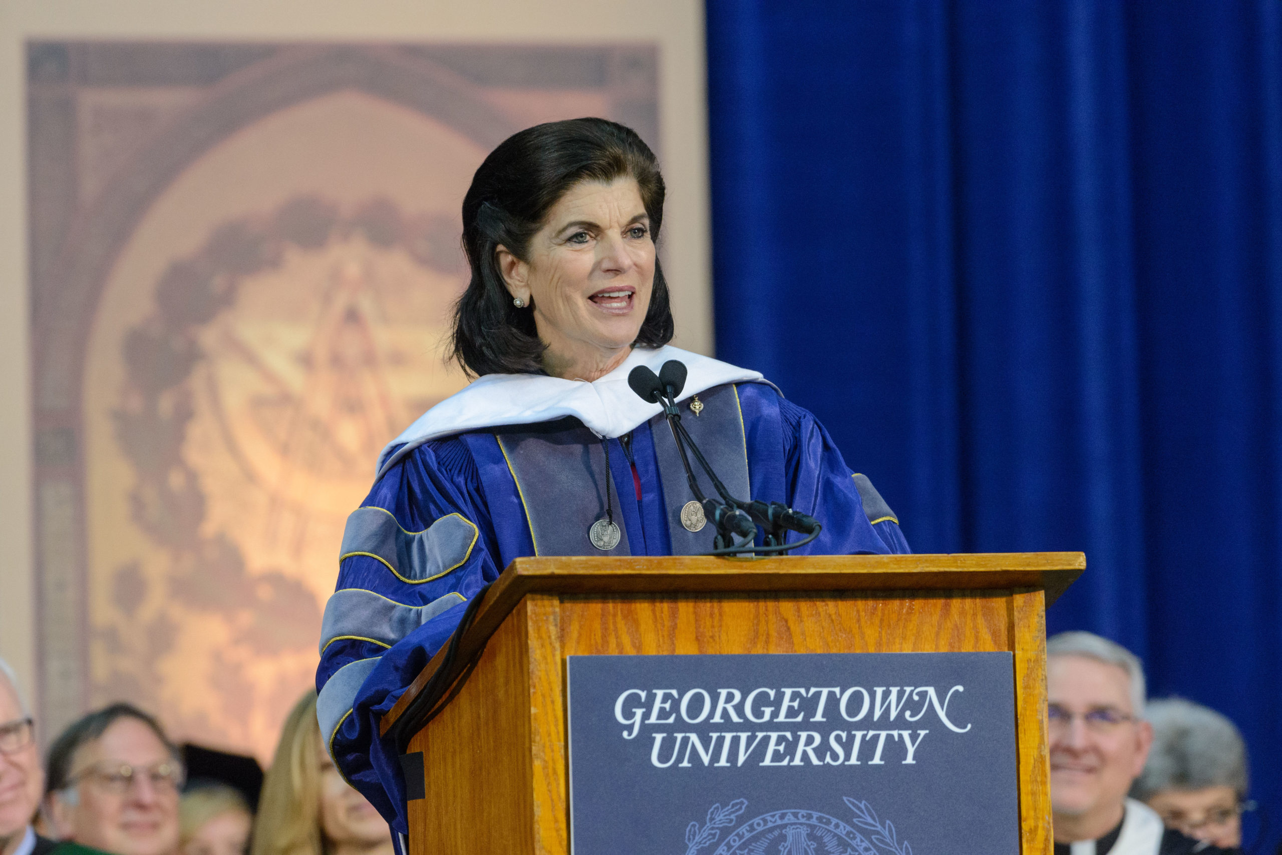 Luci Johnson, in academic regalia, speaks at a podium in McDonough Arena at Commencement 2018