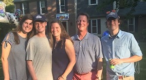 Carolyn Gugerty Hrdlick and family stand in front of a house together for a photo in casual summer attire.