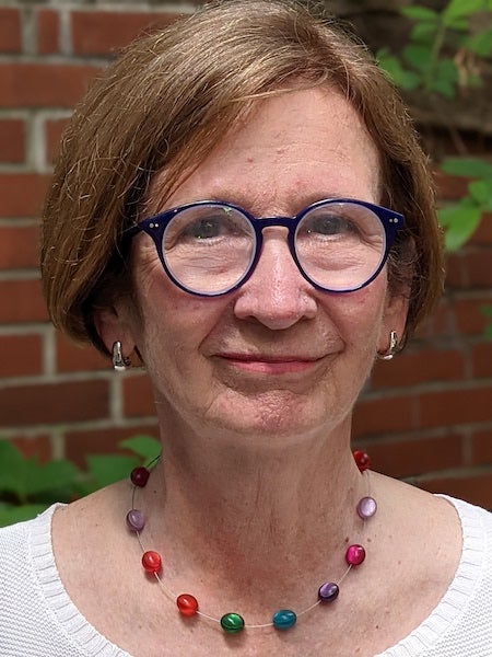 Dr. Patricia Cloonan in a portrait-style photograph outdoors with a brick wall and plants behind her.
