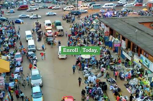 A photograph of a city street with cars and an urban market with the words "Enroll Today."