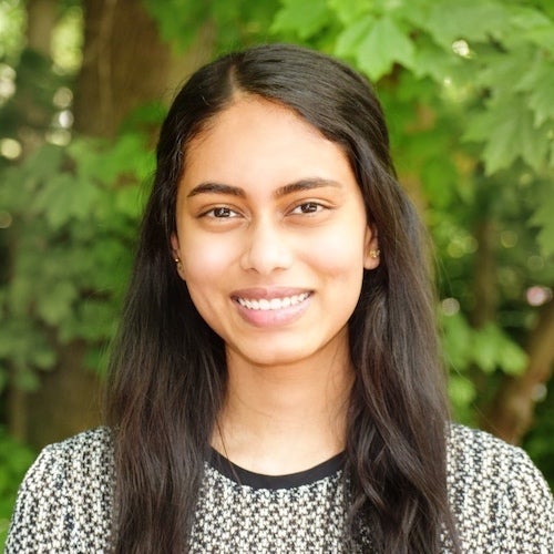 Sannidhi Shashikiran (NHS'22) poses for an official portrait style photograph in front of green foliage in an outdoor setting.