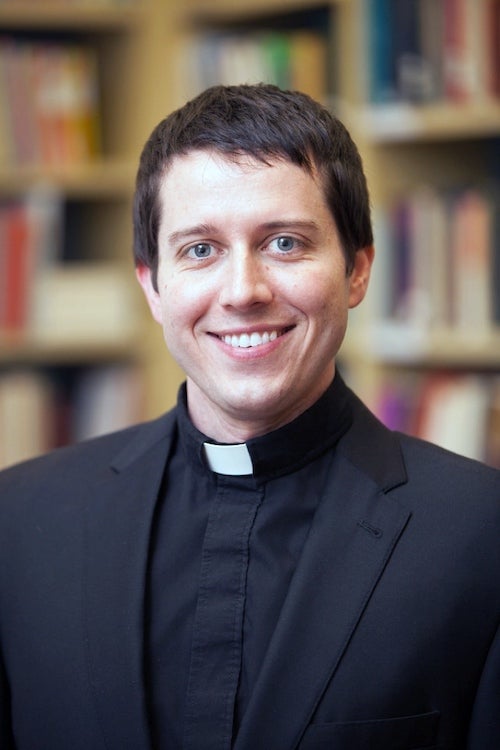 Father Michael Rozier, pictured in front of bookshelves, in his clerical collar.