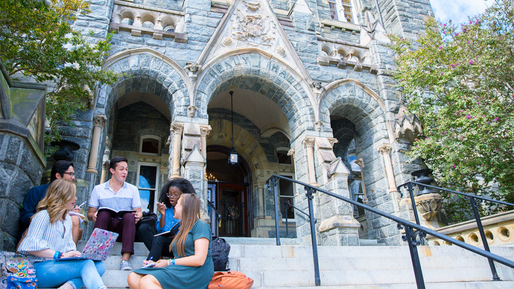 A group of students sit on the stairs of Healy Hall