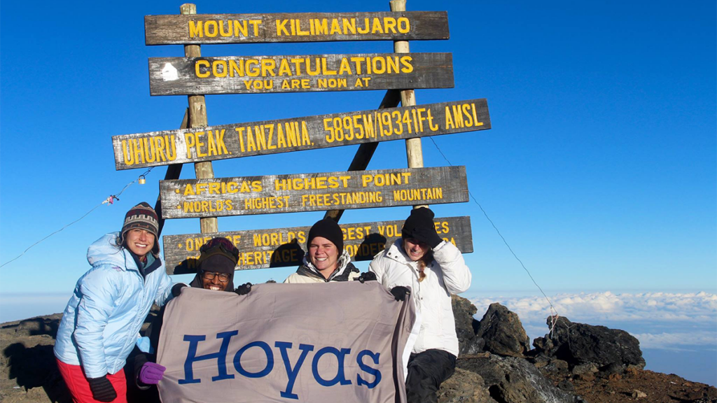 Several students sit with a Hoya banner atop Mount Kilimanjaro