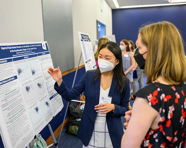 (r to l) Jan LaRocque, PhD, Undergraduate Research Conference co-advisor, listens as Binqi Chen, a student in the Human Science Program, presents her research.