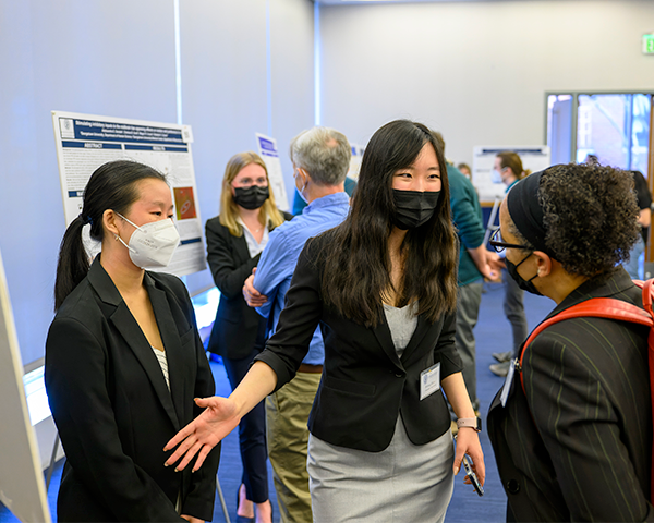 Student Britney Shaw (pictured center) discusses her poster with conference keynote speaker Eve De Rosa, PhD (right).