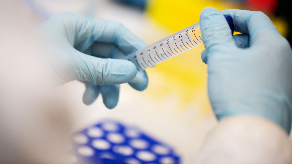 Gloved hands hold a test tube in a lab