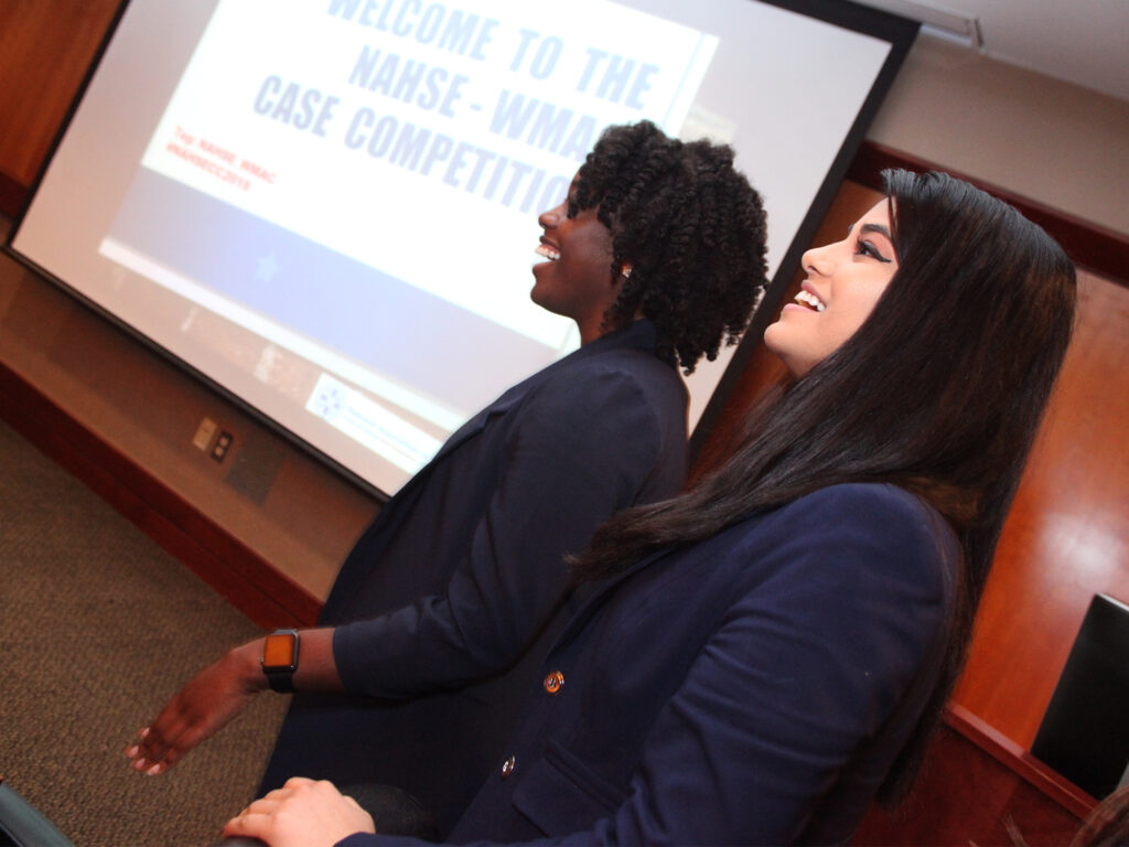 Two students stand before a screen while giving a presentation