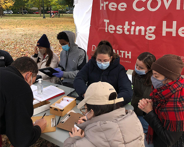Student volunteers wearing masks help sign in people seeking screening for COVID