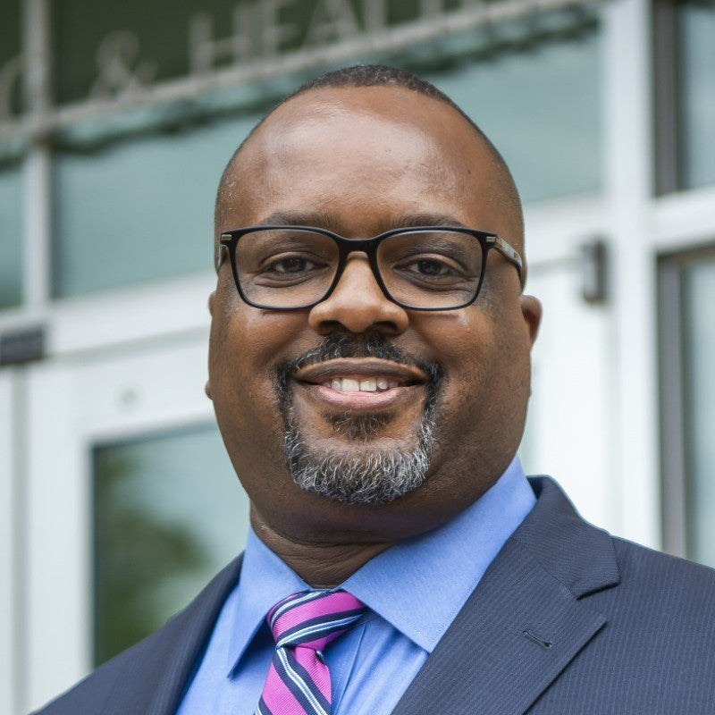 Dr Derek Griffith headshot in front of School of Health building