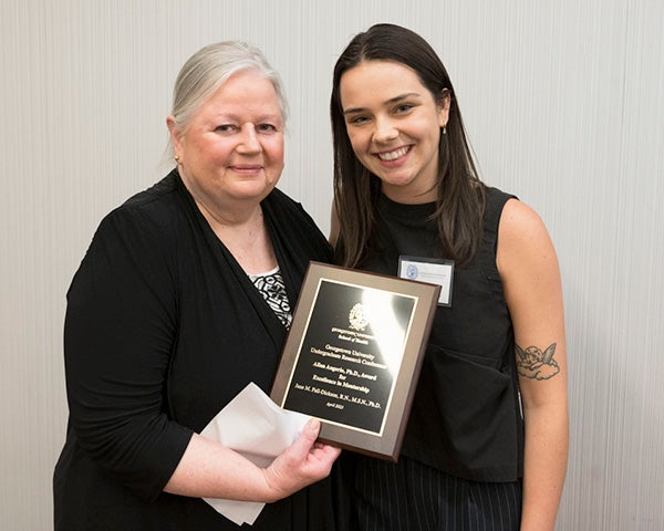 Two people stand side by side, one holding an award