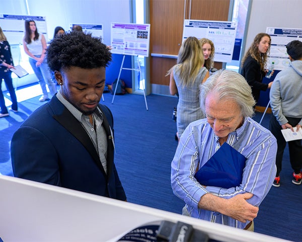 A student discusses his poster with a professor