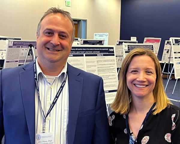 Two people stand together in a room filled with academic posters