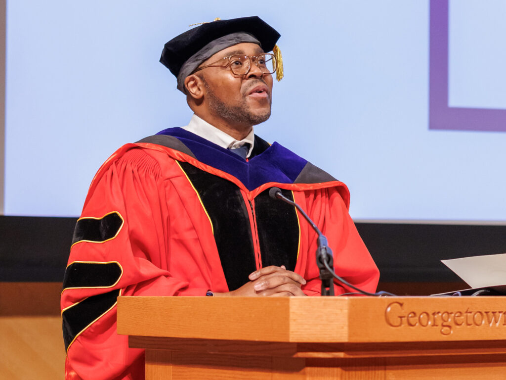 Christopher King in academic regalia speaks from a podium