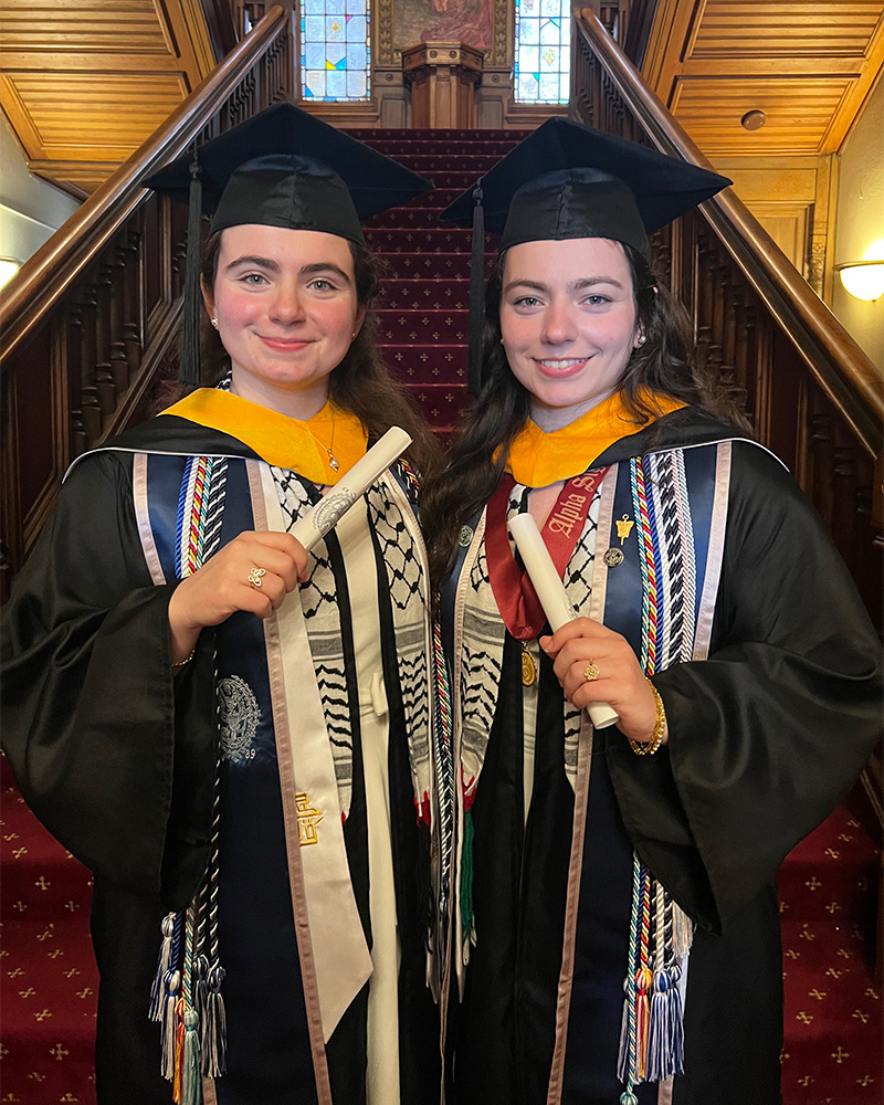 Layan and Nesreen stand on a staircase in their graduation regalia