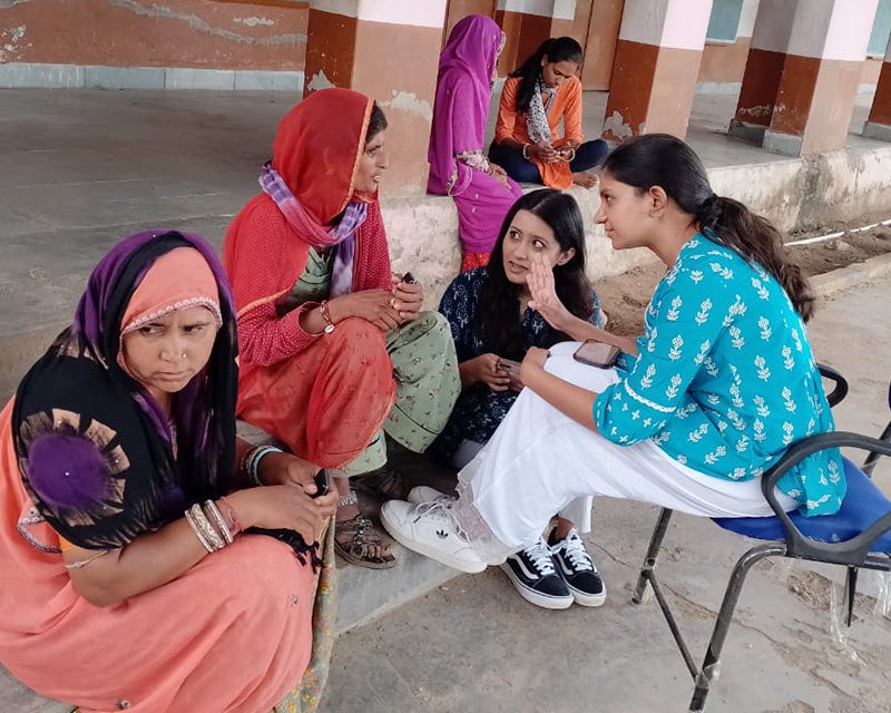 Women in India sit together and converse with Georgetown students from RISHI