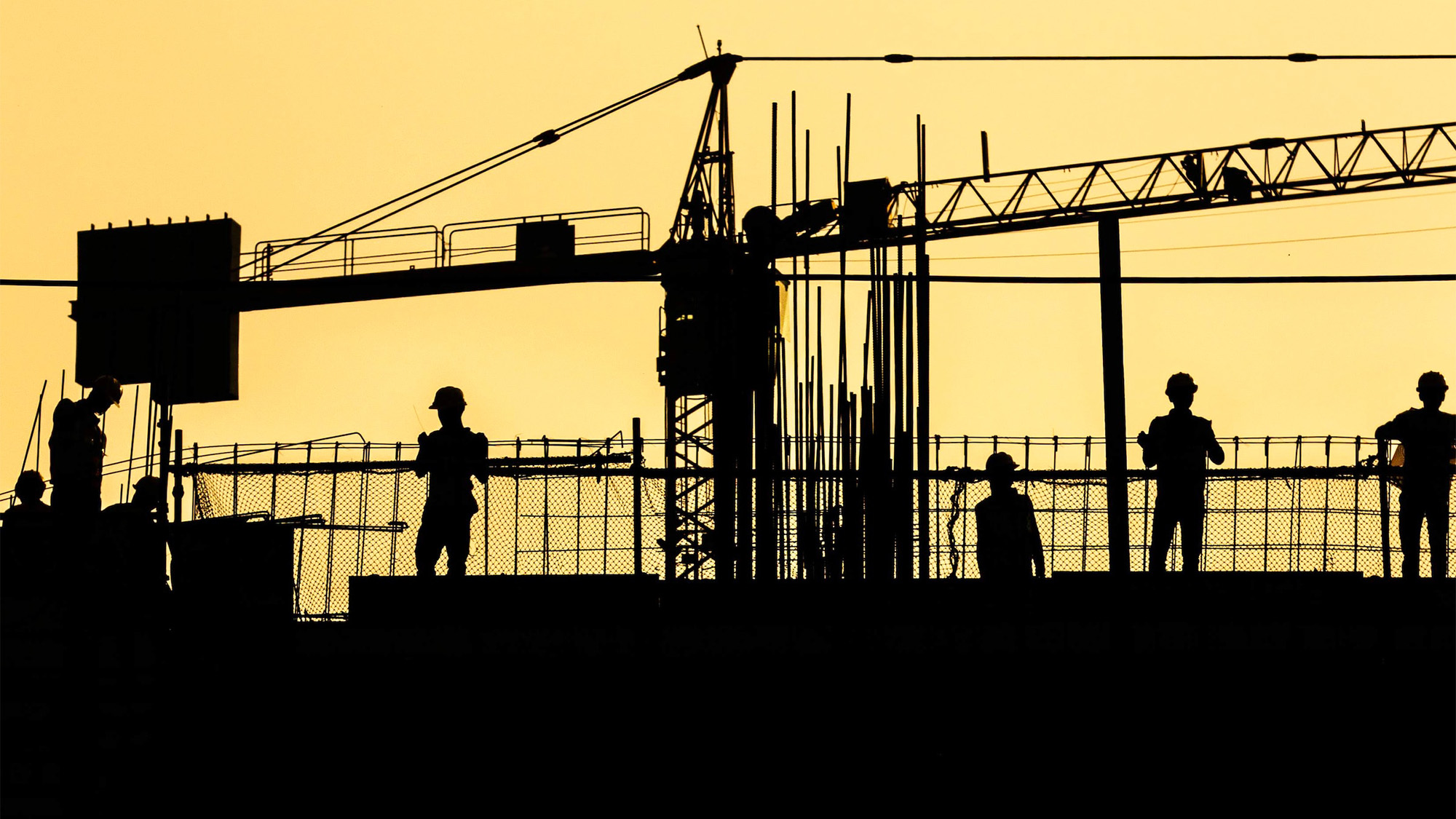 Construction workers and a crane a silhouetted against a bright yellow sky