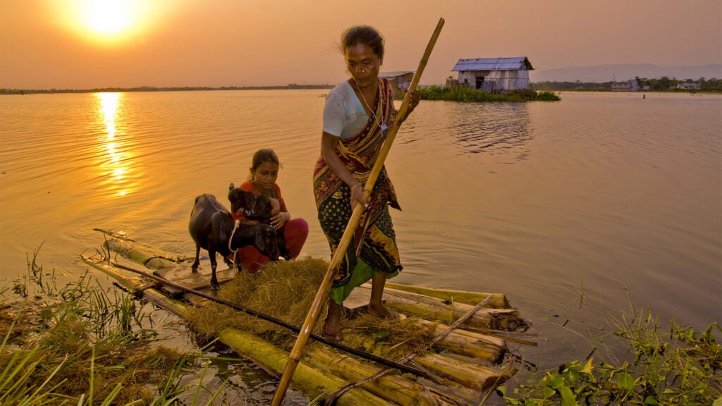 A woman on a raft in the Haor basin in Bangladesh pushes a raft on which she, a child and a goat are floating