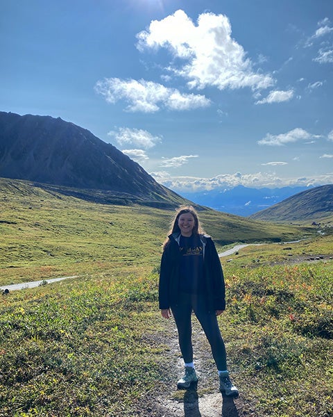 Alaina Anderson stands in a field bordered by mountains