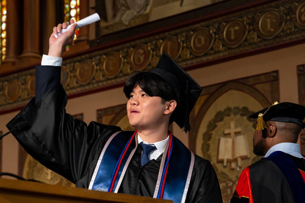 A student holds his diploma in the air in triumph