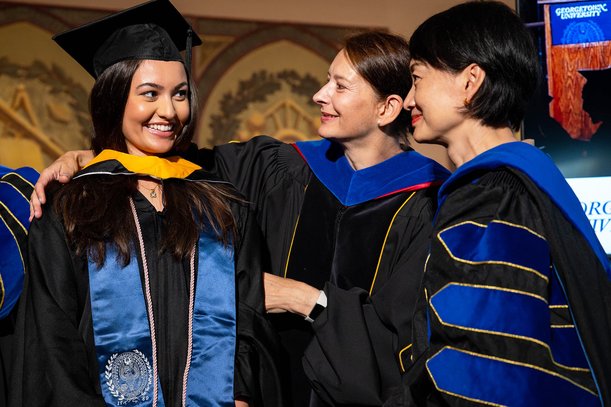 Dr. Vukovich and Dr. Bouey place a ceremonial hood on the shoulders of a master's student