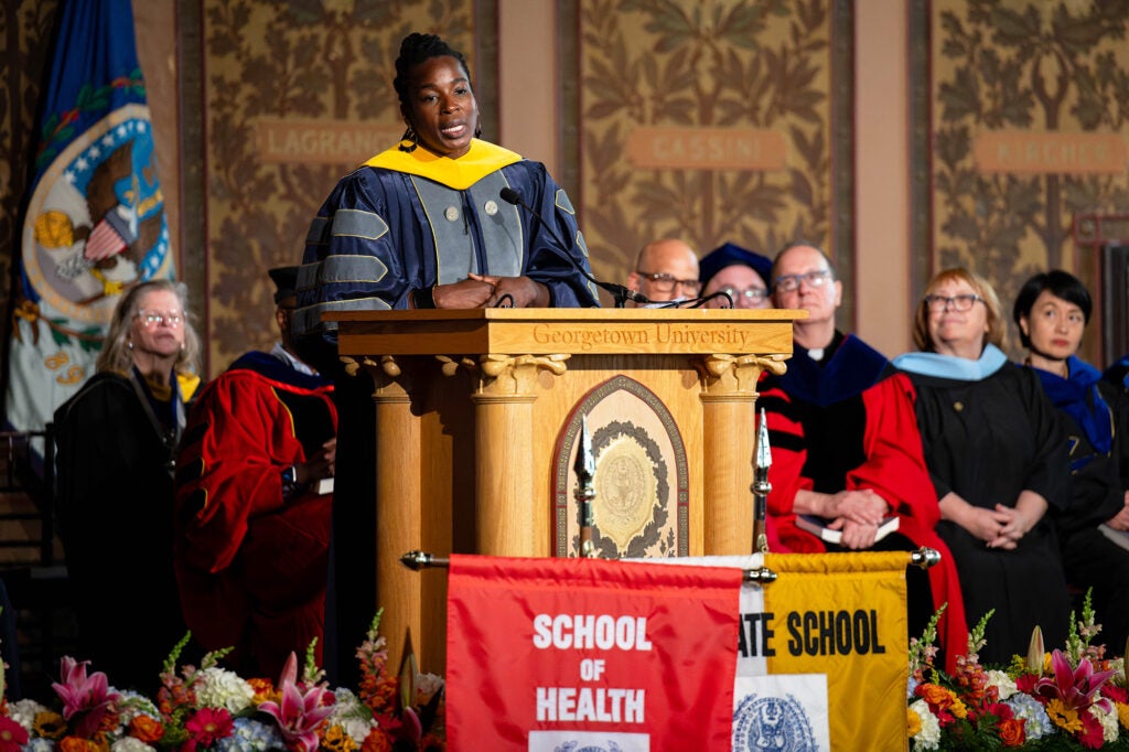 Toyin Ajayi speaks from a podium while School of Health faculty look on from their seats behind her