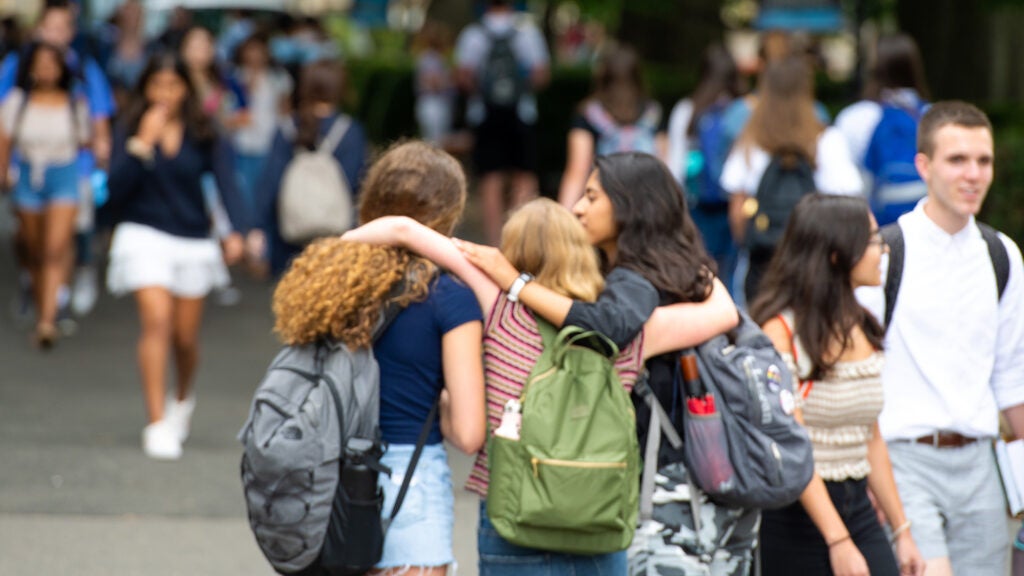 Three students viewed from the back wrap arms around each other during a GU event