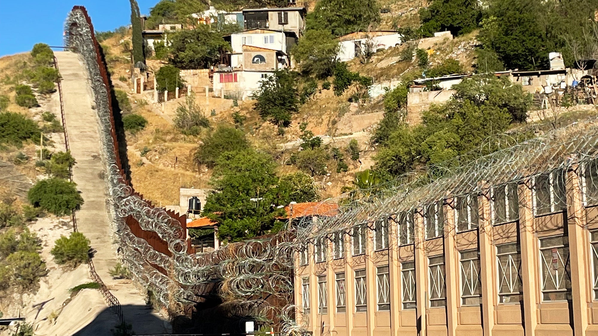 A large wall topped with razor wire stretches along a hillside