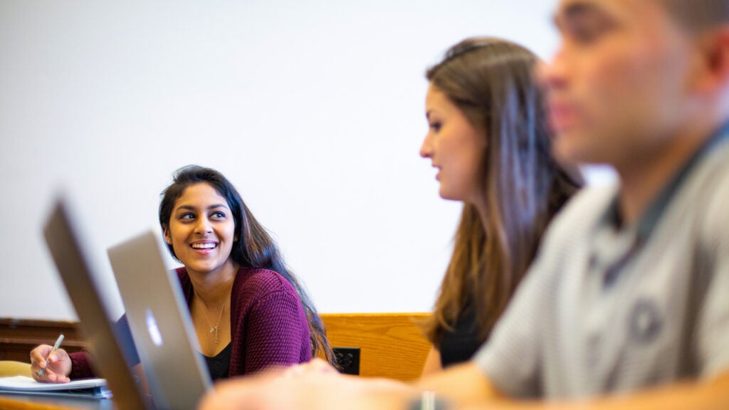 Students seated in a classroom speak with each other