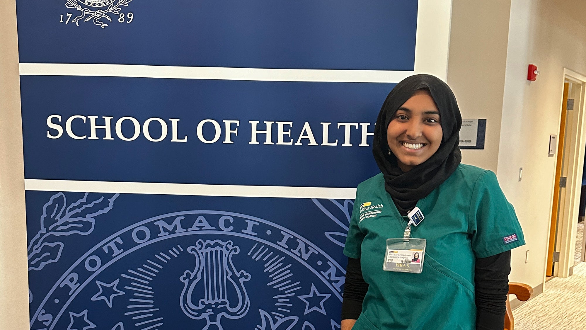 Isra Satiar stands beside a banner that reads School of Health