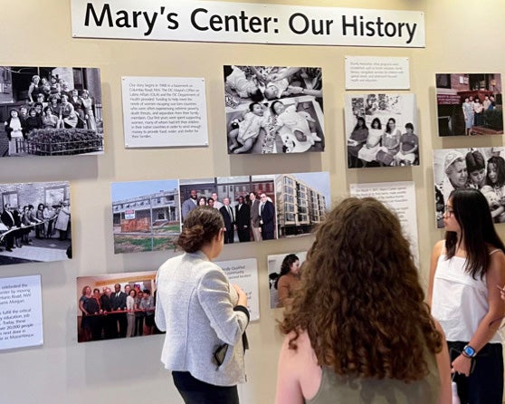 Students look at a display about Mary's Center History featuring photos and text