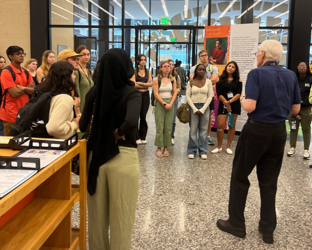 A large group of students stands in the lobby of the DC public library and listens to an employee talk about that facility