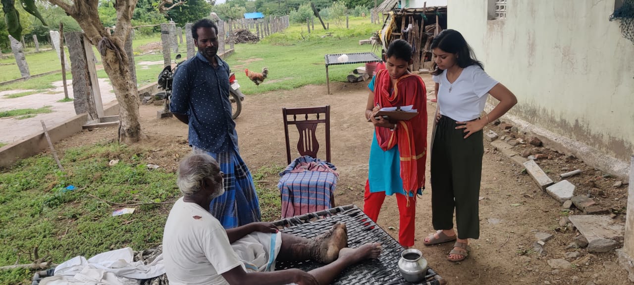A man sits on a mat while three individuals speak to him