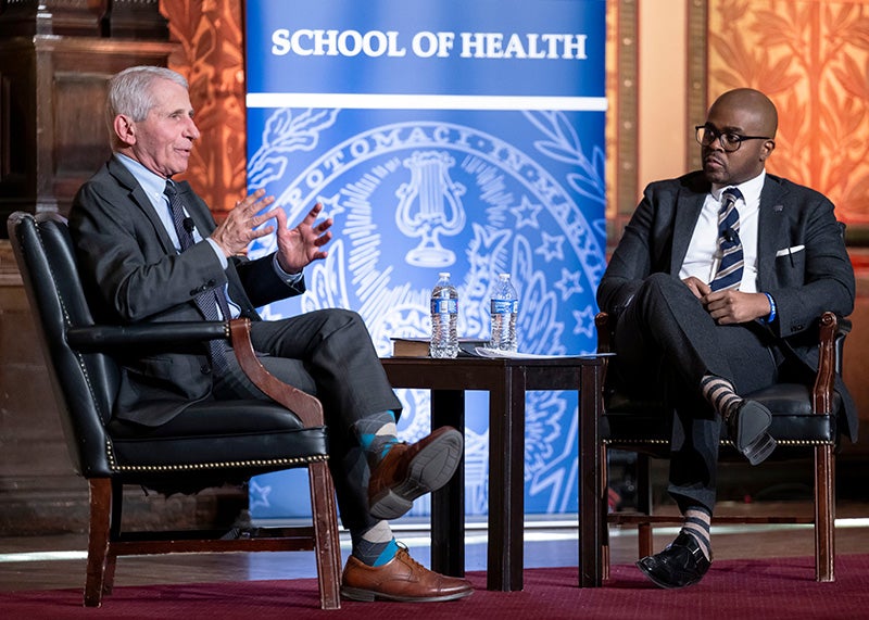 Anthony Fauci and Christopher King sit in chairs onstage in Gaston Hall