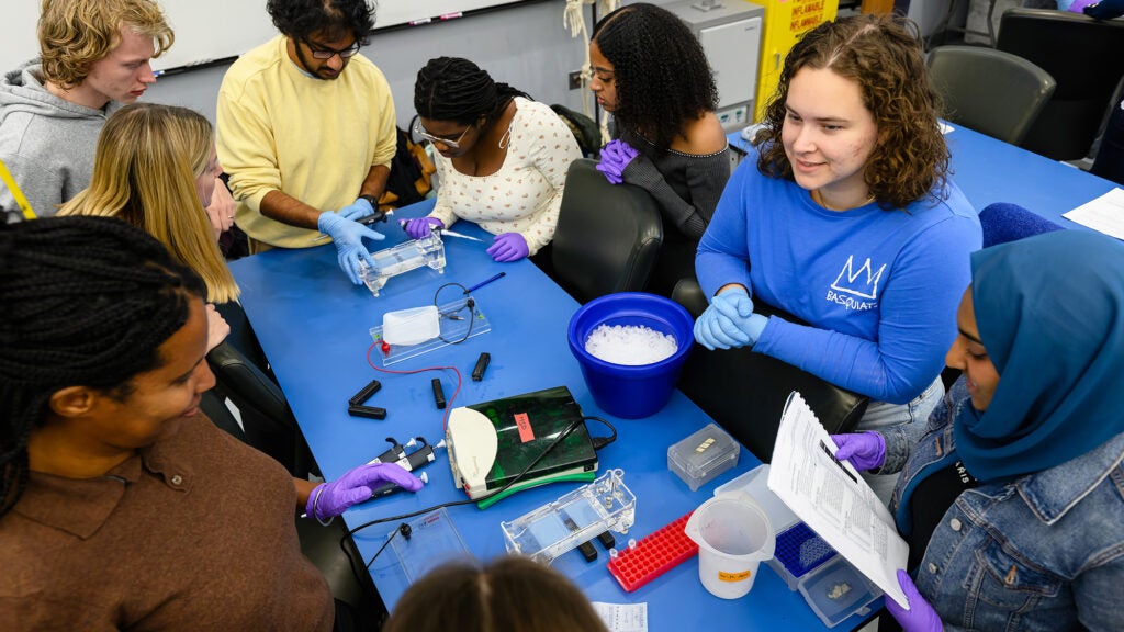 Students gather around a table filled with equipment to work their lab assignment