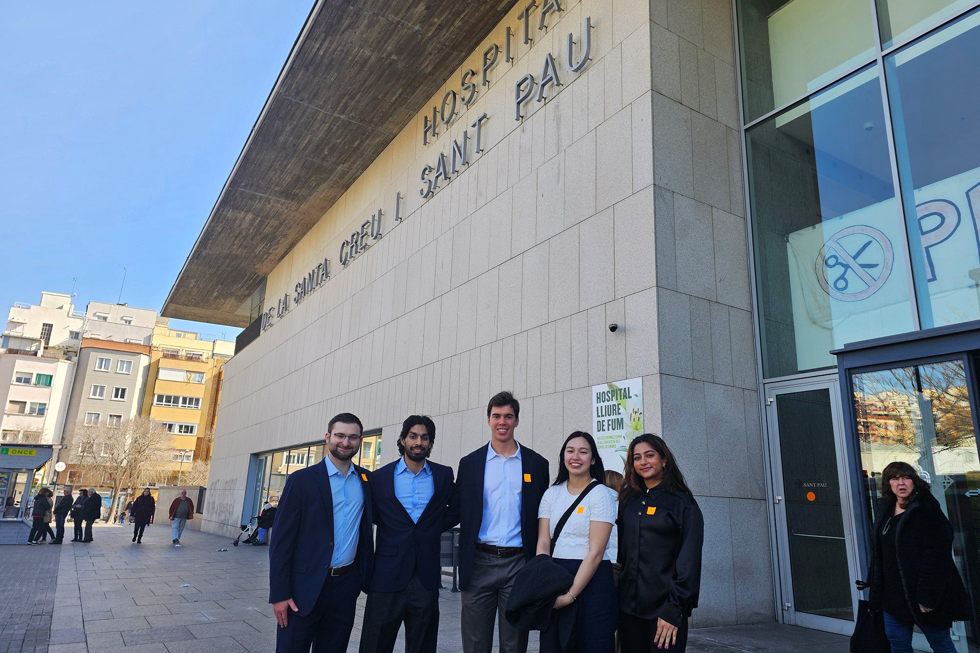 A group of five students stands outside the front entrance to the Hospital Sant Pau