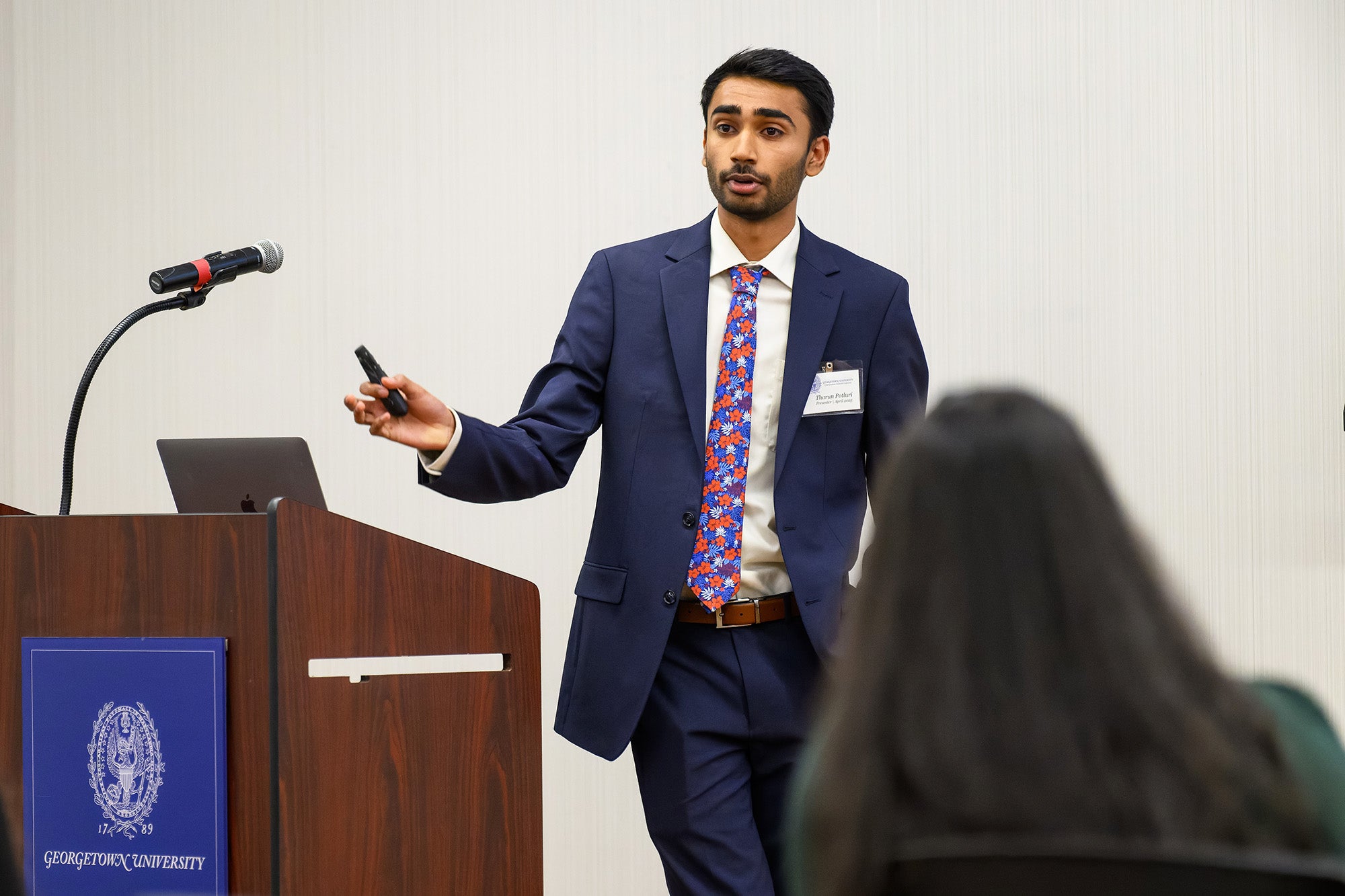 A young man wearing a suit and tie speaks from behind a podium to an audience before himi