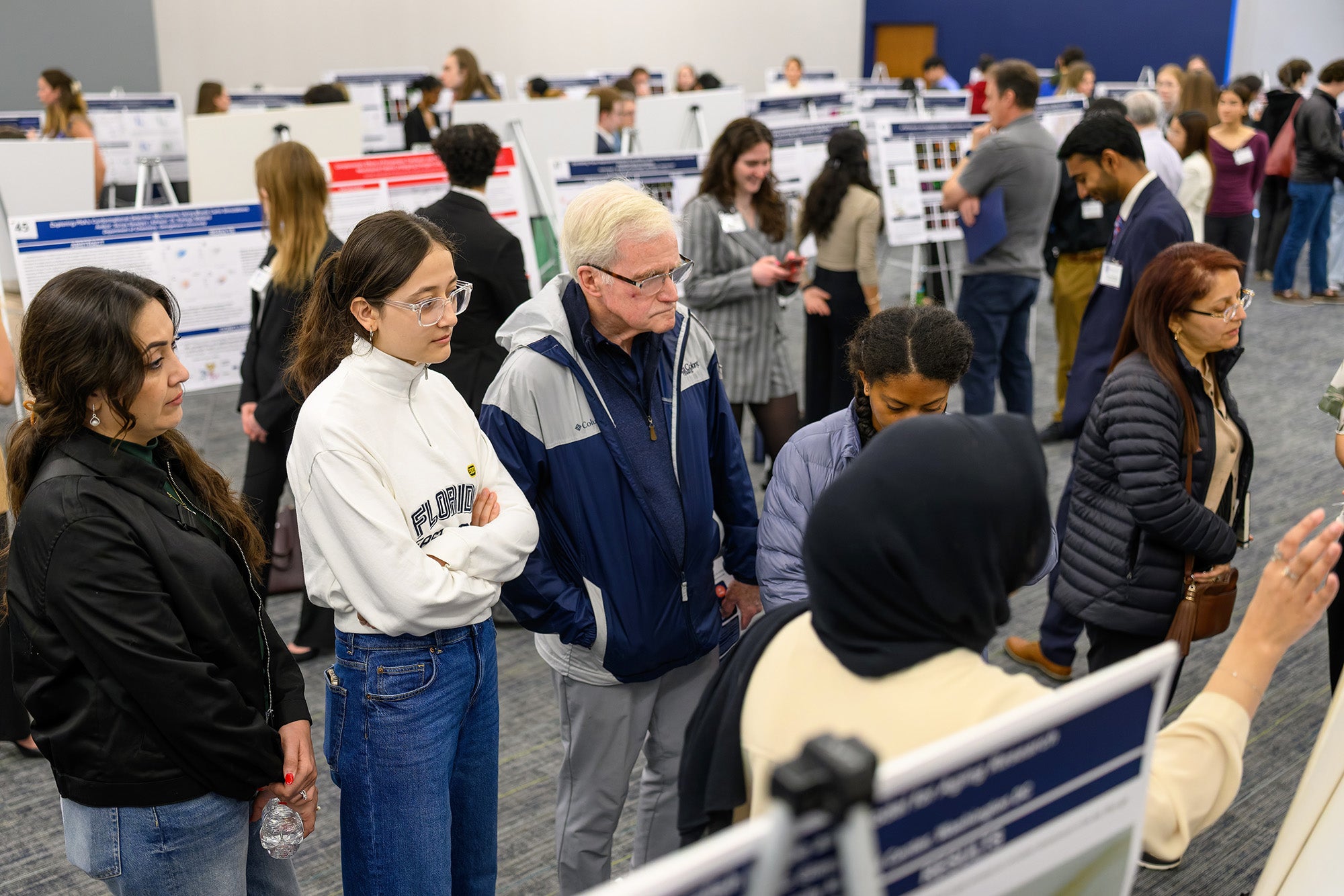 Faculty and students listen as poster presenters talk about their research