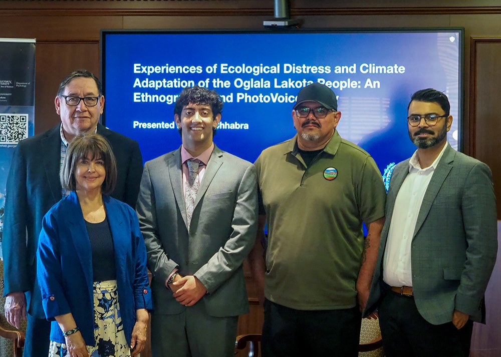 A group of five people stand together before a presentation screen