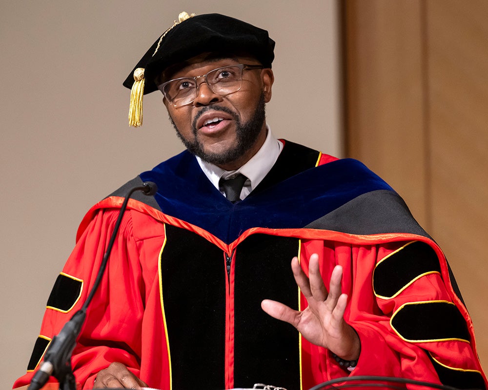 Christopher King, dressed in academic regalia, speaks from a podium
