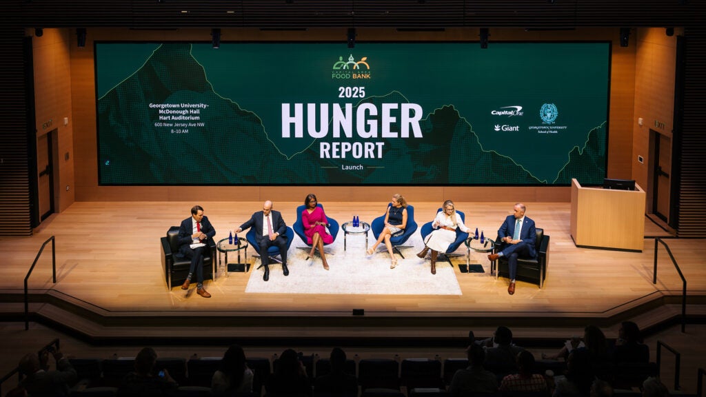 Several individuals are seated in chairs onstage at an event for the 2025 Hunger Report release