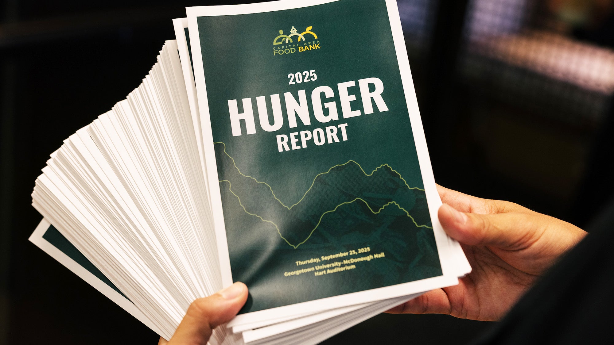 Hands hold a stack of printed Hunger Reports
