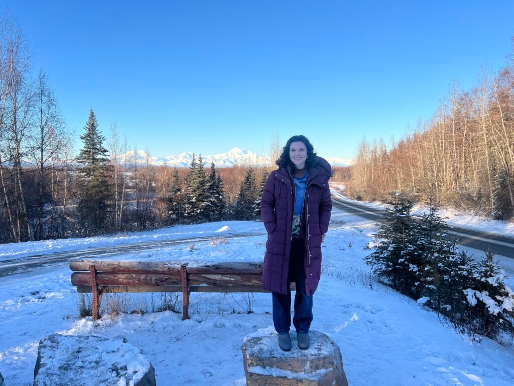 Student standing on tree stump in Alaska with Mt. Denali in the background