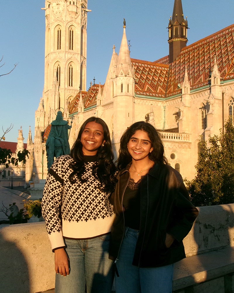 Dhruvi Parikh and Nitya Nalamothu stand together with a cathedral behind them