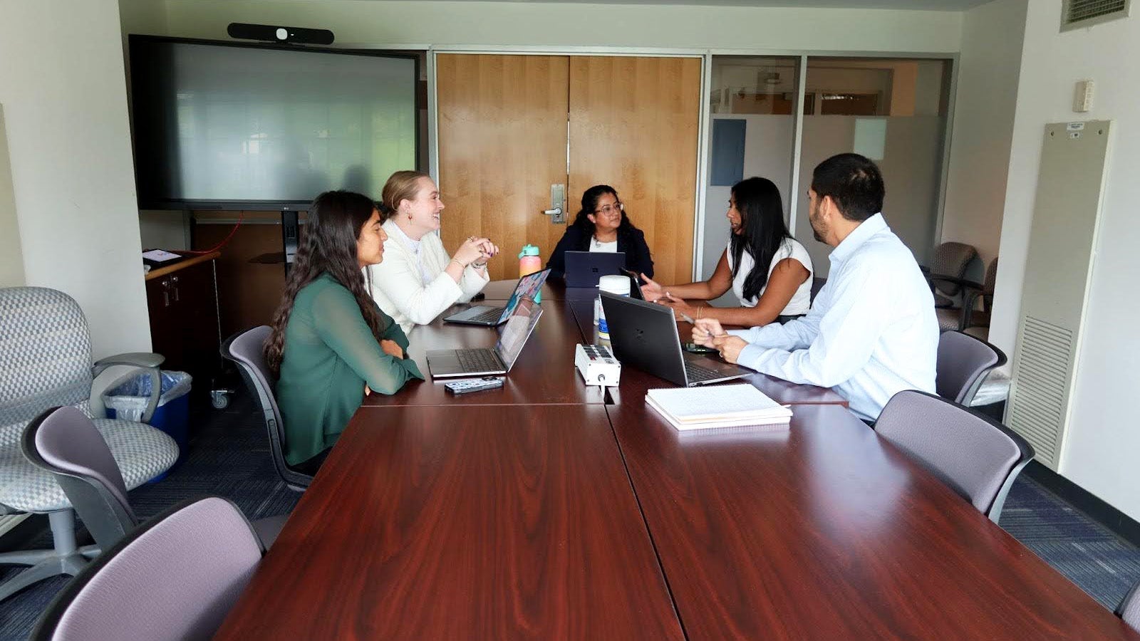 Four students converse with a professor at a table