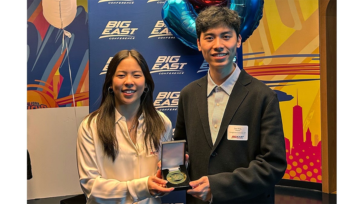 Two student stand together holding an award