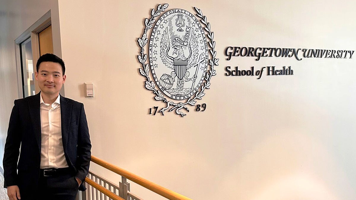 Dr. Kim stands next to the School of Health logo on the wall of a corridor