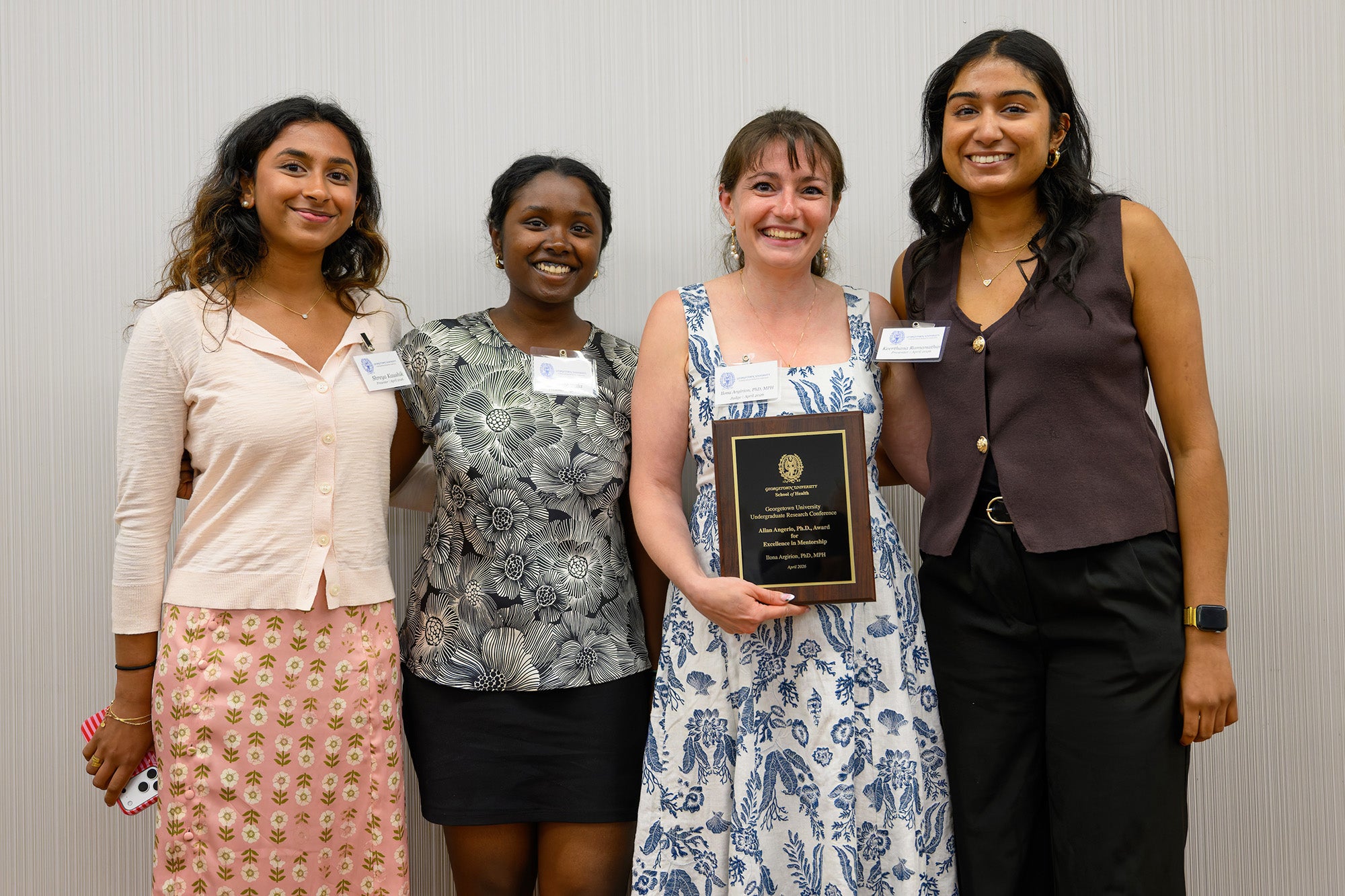Ilona Argirion holds her award plaque and stands with three students