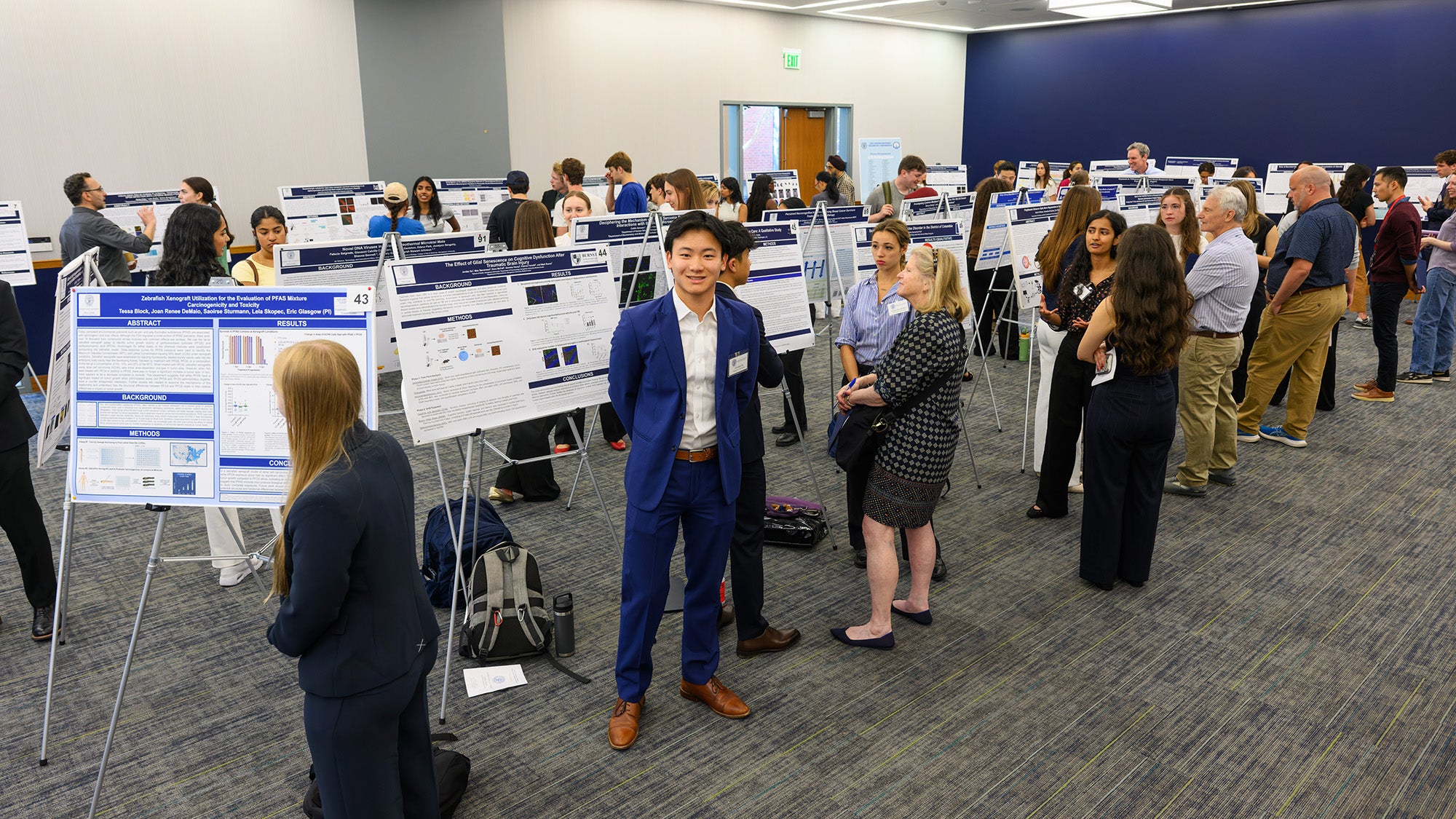 Students stand with their research posters while attendees mill around them