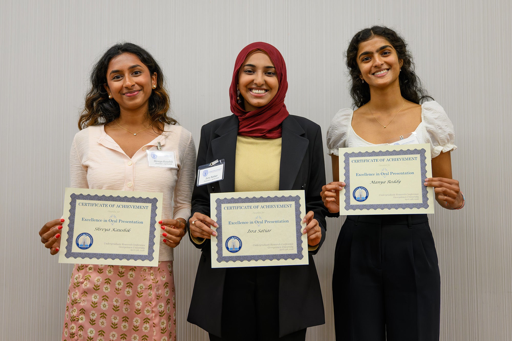 Three students stand together holding their award certificates